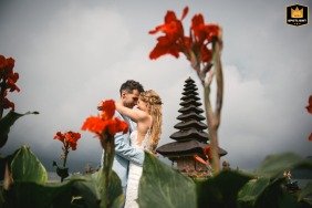 Couple hugging among flowers in Bali, Indonesia, with bright red blooms in the foreground.